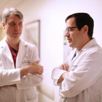 Two doctors speak to each other in a hospital hallway.
